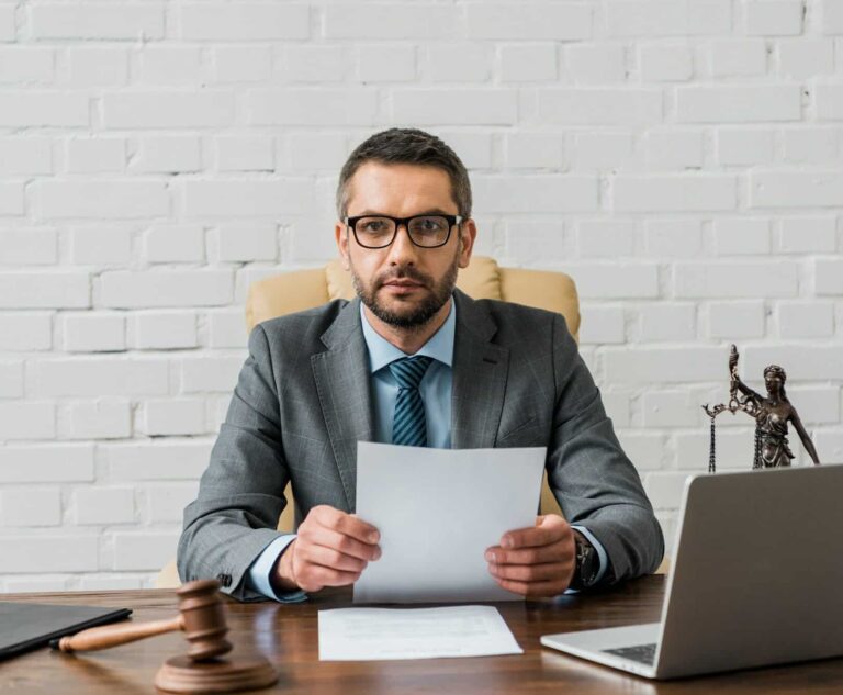 serious lawyer in eyeglasses working with papers and looking at camera in office e1666440692618